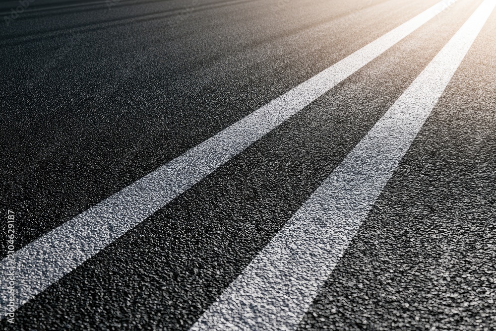Fototapeta premium Black asphalt road with two white painted lines, sunlight glinting