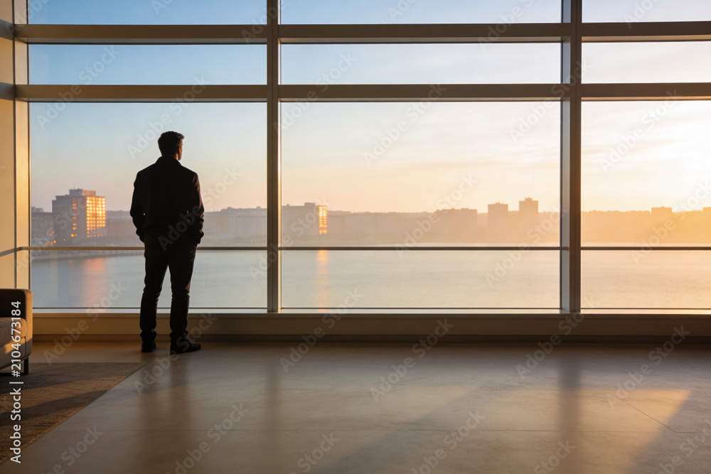 Fototapeta premium Man in suit looking out window at sunrise over city skyline