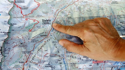 Hand pointing to a topographic map of Stelvio National Park in the Italian Alps. A person's hand indicates a specific location on a detailed topographical map of the mountainous Stelvio National Park 