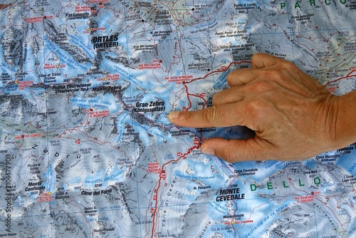 Hand pointing to a topographic map of Stelvio National Park in the Italian Alps. A person's hand indicates a specific location on a detailed topographical map of the mountainous Stelvio National Park 