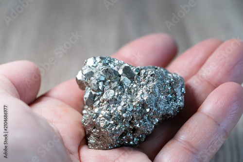 Fényképezés Piedra Pirita natural sobre la palma de una mano, primer plano de mineral plateado dorado brillante, símbolo de abundancia, energía y protección