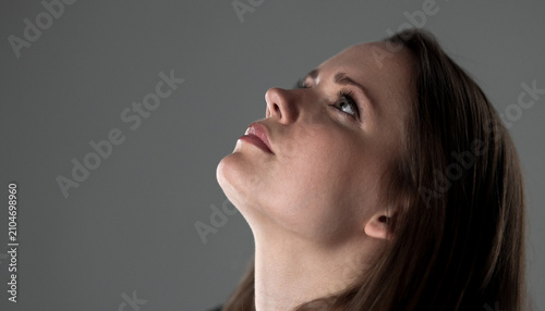 Schilderij op canvas Woman in profile looking up against a gray background, contemplating hope and th
