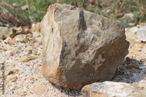 Large rough stone boulder resting on sandy ground at outdoor construction and excavation site