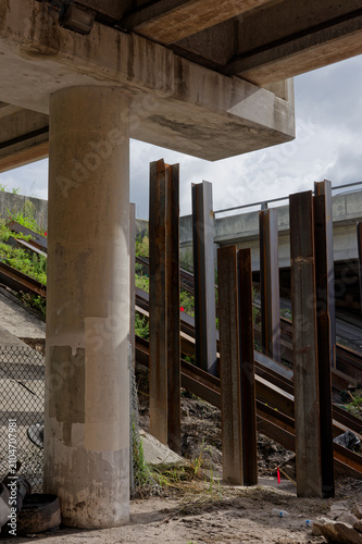 Konstfotografi Underneath a concrete overpass, rusted steel piles and vertical support beams li