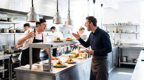 Chef and waiter arguing in a busy restaurant kitchen