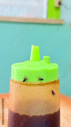 Houseflies crawling on green condiment bottle in a restaurant