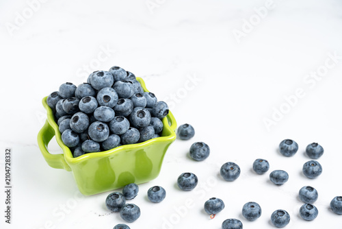 Fotografía Fresh picked blueberries in a bright green basket shaped ceramic bowl on a white