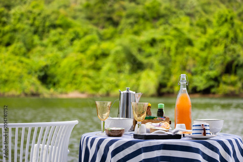 Breakfast and orange juice beside a calm forest lake.