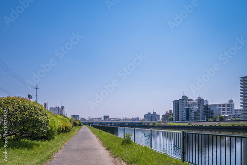 青空の下に続く川沿いの遊歩道と街並みの景色