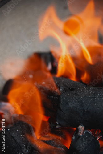 Fotografie Hot orange flames licking at black charcoal briquettes, creating a warm, fiery g