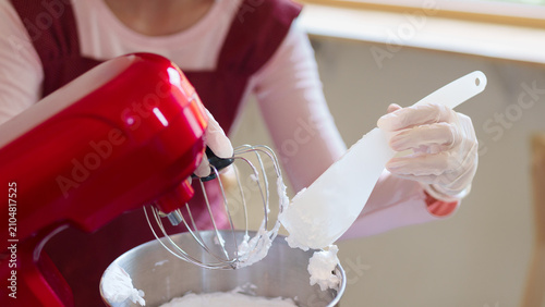 Foto Woman using spatula to add white frosting from red stand mixer into bowl during