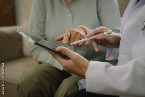 Doctor reviewing digital medical information with a senior patient on a tablet during a home healthcare consultation.