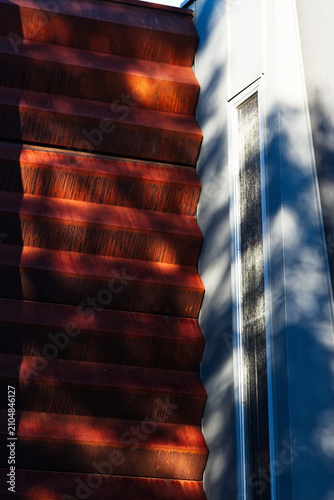 Bild auf Leinwand Dappled sunlight on ridged rusty metal facade