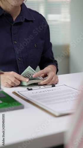 Realtor counting a stack of hundred-dollar bills at the office desk. A client is making a cash payment for a property after signing the contract.