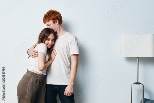 Foto Young couple embracing tenderly near white wall in casual clothes indoors, showing affection and closeness in cozy home environment with soft lighting and relaxed mood