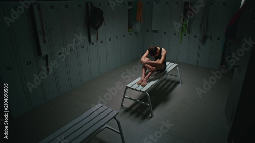 Depressed or Exhausted Teenage Athlete Sitting Alone on Bench, Hugging Knees With Arms. Girl Experiences Moment of Psychological Burnout, Pressure, Failure, or Deep Fatigue After Hard Workout.