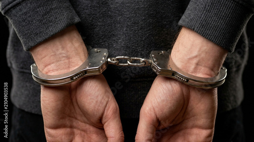 Close-up of hands in handcuffs against a dark background - crime, arrest, justice concept