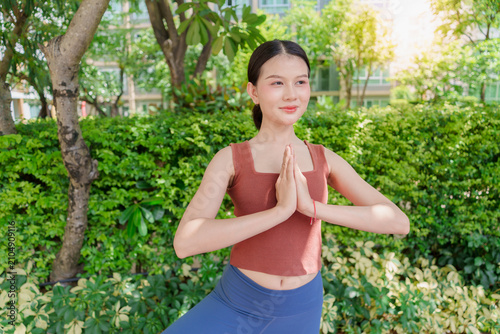 Quadro su tela Asian Gen Z woman practicing standing yoga pose in urban park promoting wellness