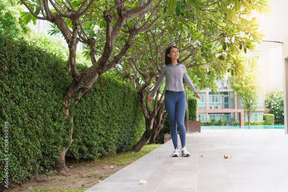 Fototapeta premium Asian Gen Z woman stretching body and twisting after workout in green urban park for wellness healthy lifestyle and fitness.