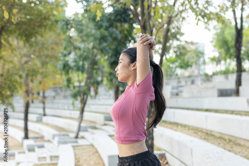 Fotografie Young calm asian woman wearing pink activewear performing fitness stretch outdoo