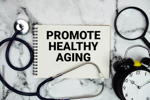 Promote Healthy Aging text written on notepad with stethoscope and magnifying glass on marble background