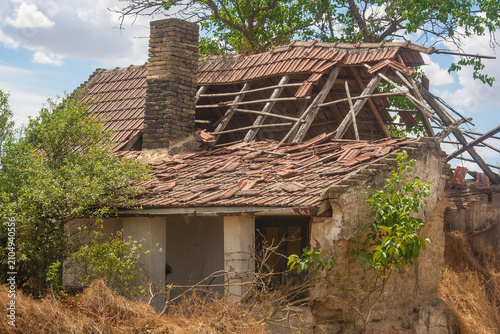 Billede på lærred An abandoned house with a damaged roof and overgrown vegetation