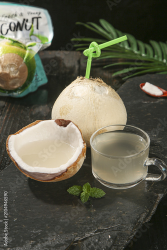 Fresh Coconut Water Drink with Green Straw and Tropical Leaves on Dark Slate Background