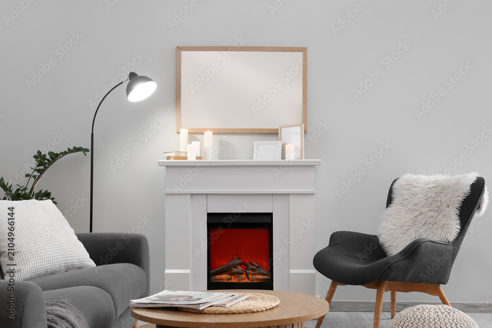 Obraz premium Cozy living room interior with a modern electric fireplace, comfortable gray sofa, and armchair with a fluffy pillow