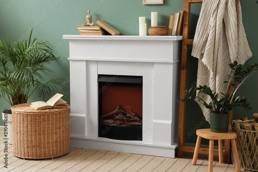 Obraz premium White electric fireplace with decorative mantel in a cozy living room interior with green walls and plants