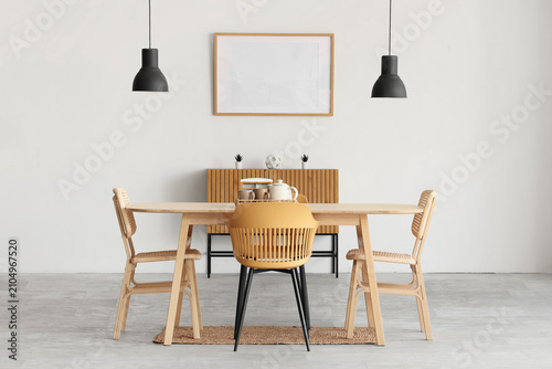 Foto Interior of light room with blank frame, commode and dining table