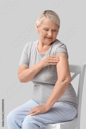 Senior woman with medical patch after vaccination sitting in chair on light b...