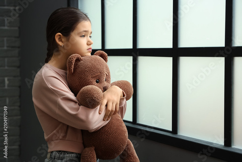 Sad girl with toy bear near...