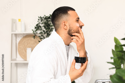 Young man applying cream on...