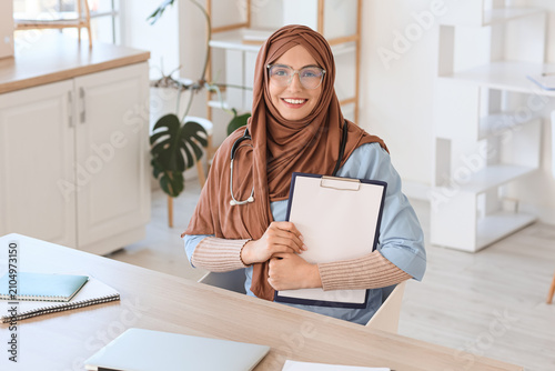 Female Muslim doctor in hijab with clipboard sitting at hospital