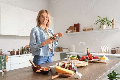 Young woman making tasty tacos at table in kitchen