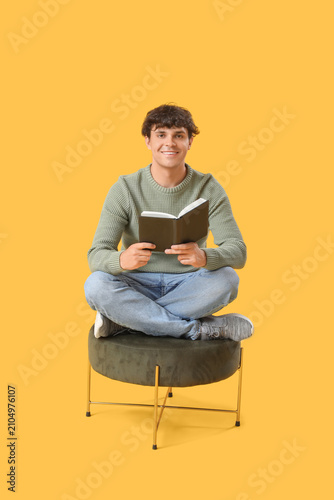 Young man reading book on pouf against yellow background