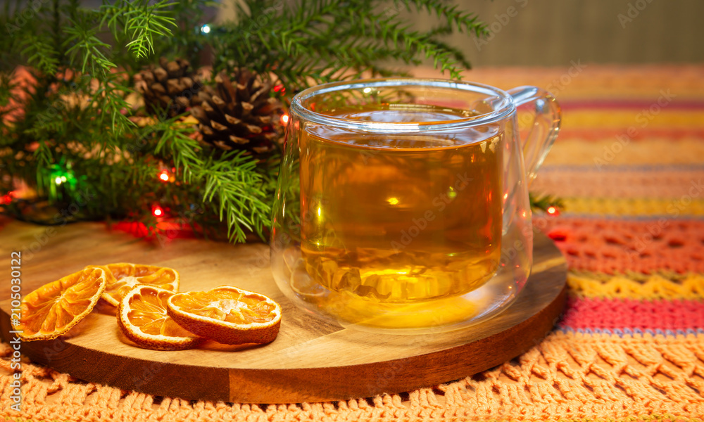 Fototapeta premium Cozy Christmas still life with green tea and dried oranges on a wooden board over a crocheted tablecloth