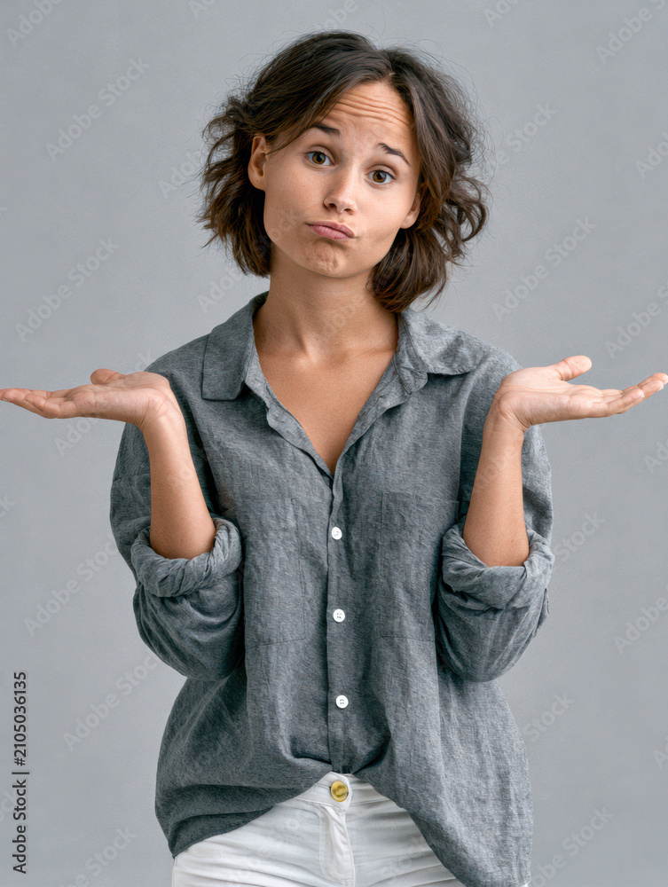 Obraz premium Young woman shrugging hands, casual gray shirt, white pants, neutral background, uncertain expression, short brown hair, studio portrait