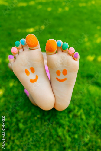 Bild auf Leinwand Child feet with painted colorful toes and happy smileys on green grass