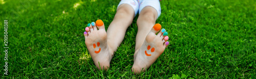 Child feet with painted colorful toes and happy smileys on green grass.
