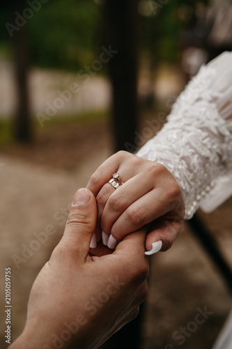 Groom's hand holding bride's hand in white dress with gold wedding ring on finger