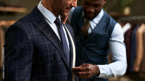 A man wearing a tailored suit while another person measures his jacket for fit and precision