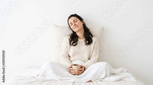 Peaceful woman sitting in bed with a warm drink