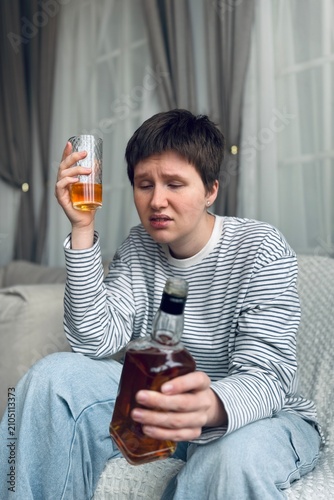 Woman holding glass and bottle of alcohol, in living room with curtains, with glass, bottle of alcohol, from a over-the-shoulder perspective perspective, with brown, white accents.