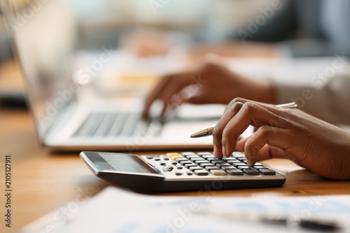 Person's hands operating a calculator and laptop in a brightly lit office setting during a financial task
