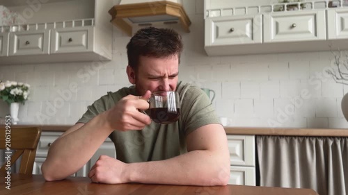 man drinking coffee and suffer kitchen setting with wooden table and ceramic pitcher, daily life scene with green shirt and brown wooden table, close-up view of man enjoying coffee in home.