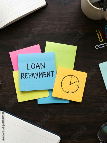 Loan repayment note written on colorful sticky notes on a dark office desk