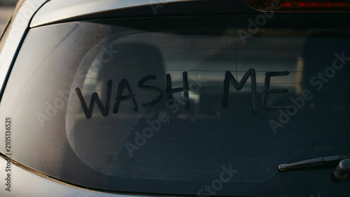 The phrase wash me written in the dust on a dirty rear car window