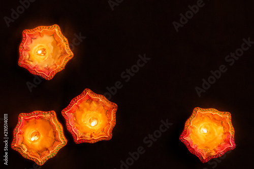 Canvas Print Four lit clay diyas burning on black background for Diwali festival of lights