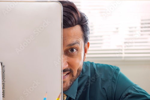 A corporate employee's face partially visible peeping out from the desktop screen in office.